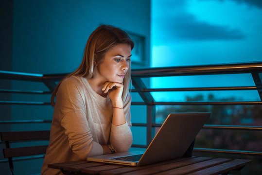 Young beautiful blonde woman working on laptop at night. High ISO image.