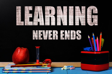 Text Learning never ends on school black chalkboard with school accessories