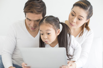 Attractive Little Girl using Laptop with Mom and Dad Together. Girl learning to use Laptop. Happy Family Concept.