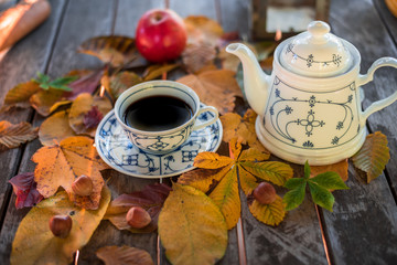 Antique coffee service in autumn on a wooden table, with yellow fall leaves and apples