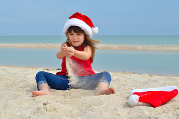 Obraz premium Cute little girl celebrating Christmas and New Year holidays on the beach, playing with sand