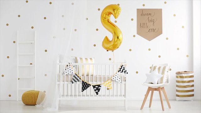 White wooden crib with pennants and big golden balloon in room for newborn