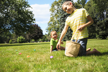 children having fun collecting Easter eggs. cheerful boys pick up colorful eggs from the grass...