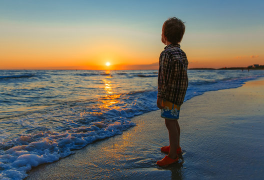 little boy watching the sunset on the beach. impressed child admires nature on the ocean shore