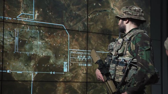 Single male bearded soldier in camouflage army uniform reviewing monitor of missle launch on large computer screen display