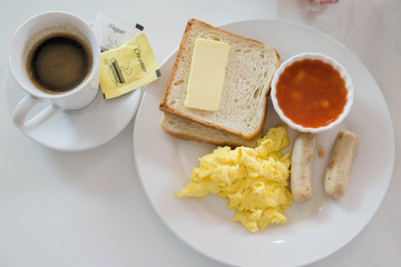 Breakfast continental set : scramble egg, sausage, toast and butter and baked beans serve with black coffee , sugar and cream