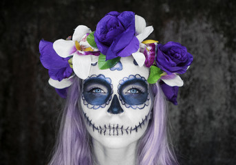 Closeup face of woman with Mexican sugar skull makeup and flowery wreath looking into the camera....