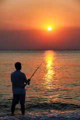 Man fishing in last rays of sunlight on sea shore