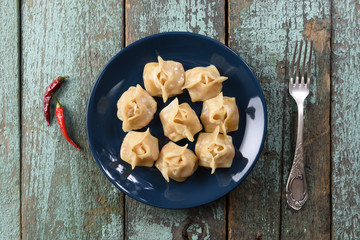 Manti or steam dumplings with chili peppers. Traditional dish of Uzbekistan in navy blue plate on shabby rustic background