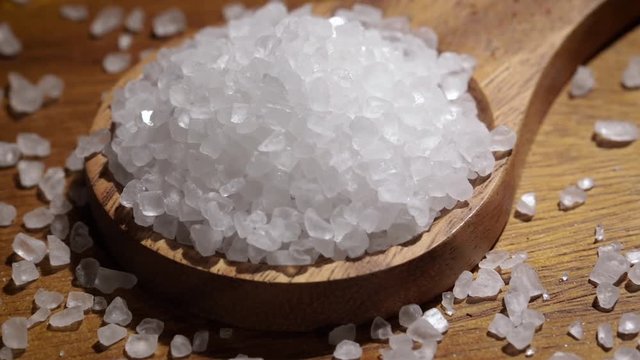 Sea salt crystals closeup in wooden spoon on a kitchen table.