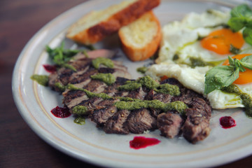 Grilled beef steak with toast , fried egg and vegetables on top with pesto sauce