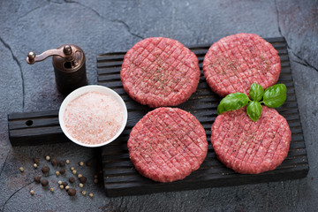 Fototapeta na wymiar Black wooden chopping board with fresh uncooked burgers made of marbled beef meat. Weathered asphalt background, studio shot