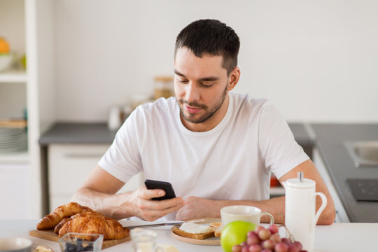 man with smartphone having breakfast at home