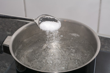 Fototapeta premium Salz in das kochende Wasser geben mit dem Löffel