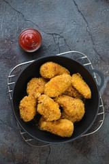 Fried chicken wings with breading served in a cast-iron pan. Cracked asphalt background, above view