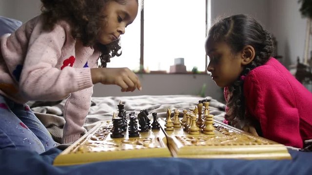 Two smart little girls playing chess on bed