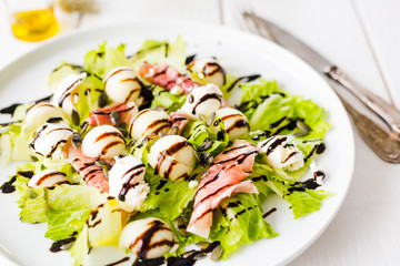 Summer Salad with Prosciutto, Melon, Cheese and Lettuce on White Wooden Background, Horizontal View