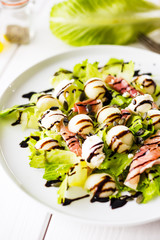 Vertical View of Arugula Salad with Melon, Watermelon, Cheese and Prosciutto on White Wooden Table
