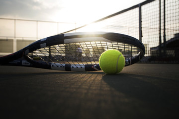 Tennis ball and racket on hard court under sunlight