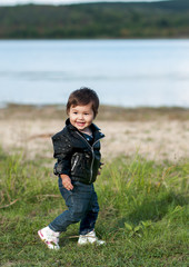 laughing baby girl in a black leather jacket, jeans and a sneaker crouching in the grass