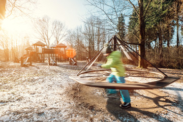 Boy turns carousel on playground in deep autumn park