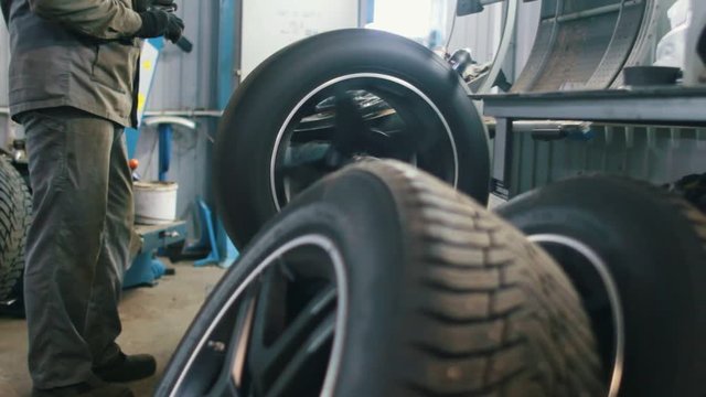 Worker in car service repairs tires - mechanical workshop
