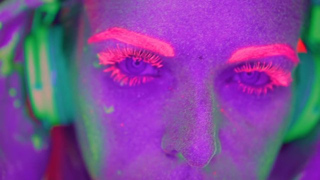 Woman face with fluorescent make up listening music with headphones, creative makeup great for nightclubs. Halloween party, shows and music video concept