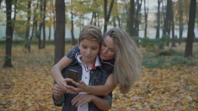 Mother and son takes selfie together at smartphone in autumn park