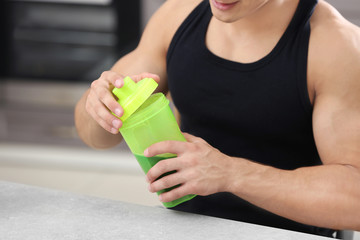 Sporty young man with protein shake in kitchen