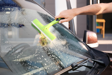 Man cleaning windscreen of car with squeegee outdoors