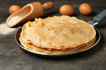 Frying pan with tasty buckwheat thin pancakes on table