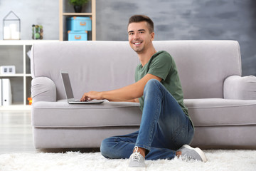 Young man with modern laptop near sofa at home