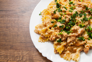 Sliced fried chicken fillet in a creamy sauce. with farfalle pasta. in plate on a wooden background. . with copy space. top view