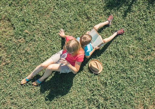 Family On Nature. Mother Drinking Water Froom Bottle. Son Reading A Book. Overhead View.