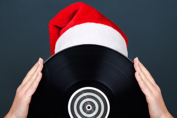 Christmas picture. A young woman in a red Santa Claus hat holds a black vinyl record for the turntable
