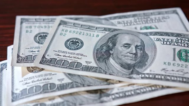 Fanned pile of hundred dollar banknotes on a table. Close-up shot