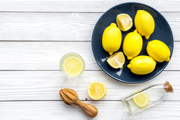 Make lemonade at home. Lemons, juicer, glass and bottle for beverage on white wooden background top view copyspace