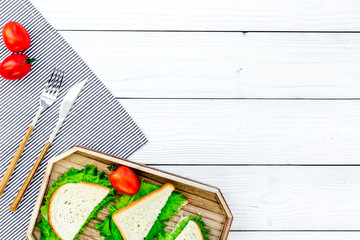 Sandwiches with lettuce for picnic on tablecloth on white wooden table background top view copyspace