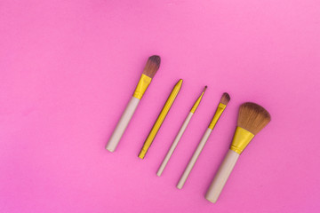 Cosmetics on colorful background. Set of brushes for makeup on pink background top view copyspace