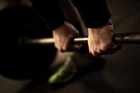 Close-up of a weight lifter in start position for sumo deadlift high pull, showing two hands on a barbell and a foot