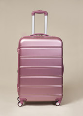 Pink trolley suitcase isolated on beige background