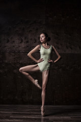 young beautiful ballet dancer in green swimsuit posing on pointes