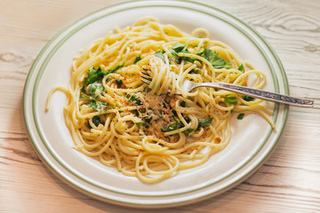 Pasta with herbs, cheese, cedar nuts on a white plate with parmesan on a light wooden background. Spaghetti with Parmesan cheese. The concept of Italian cuisine.