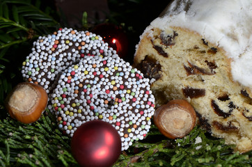Sweet German bread with raisins and icing sugar (stollen) and Christmas decoration with chocolate rings, hazelnuts, red Christmas balls and fir sprigs