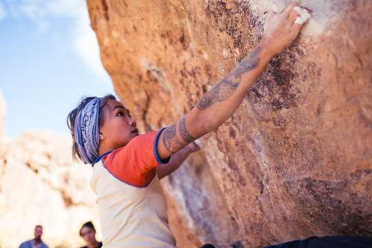 Petite Asian Woman Rock Climbing Outdoors Hangs From Stone Overhang With People Watching