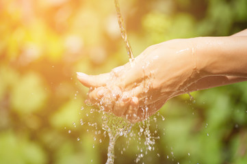 Woman washing hand outdoors. Natural drinking water in the palm. Young hands with water splash, selective focus