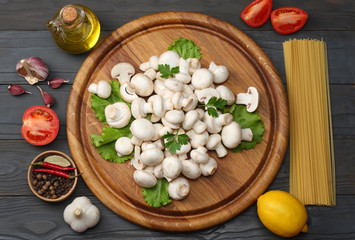 Italian food background, with tomatoes, parsley, spaghetti, mushrooms, oil, lemon, peppercorns on dark wooden table. Top view