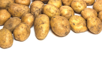 A lot of dirty potatoes on a white background. Potatoes scattered on the upper side.