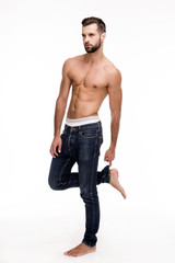 Fototapeta premium Casual and flawless. Full length of handsome young man in jeans looking away while standing against white background.