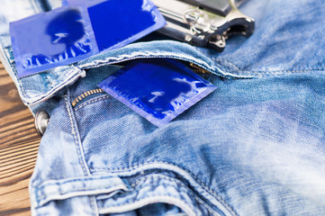 Condoms in blue package and glossy metal pistol on new blue jeans on old rustic wooden table